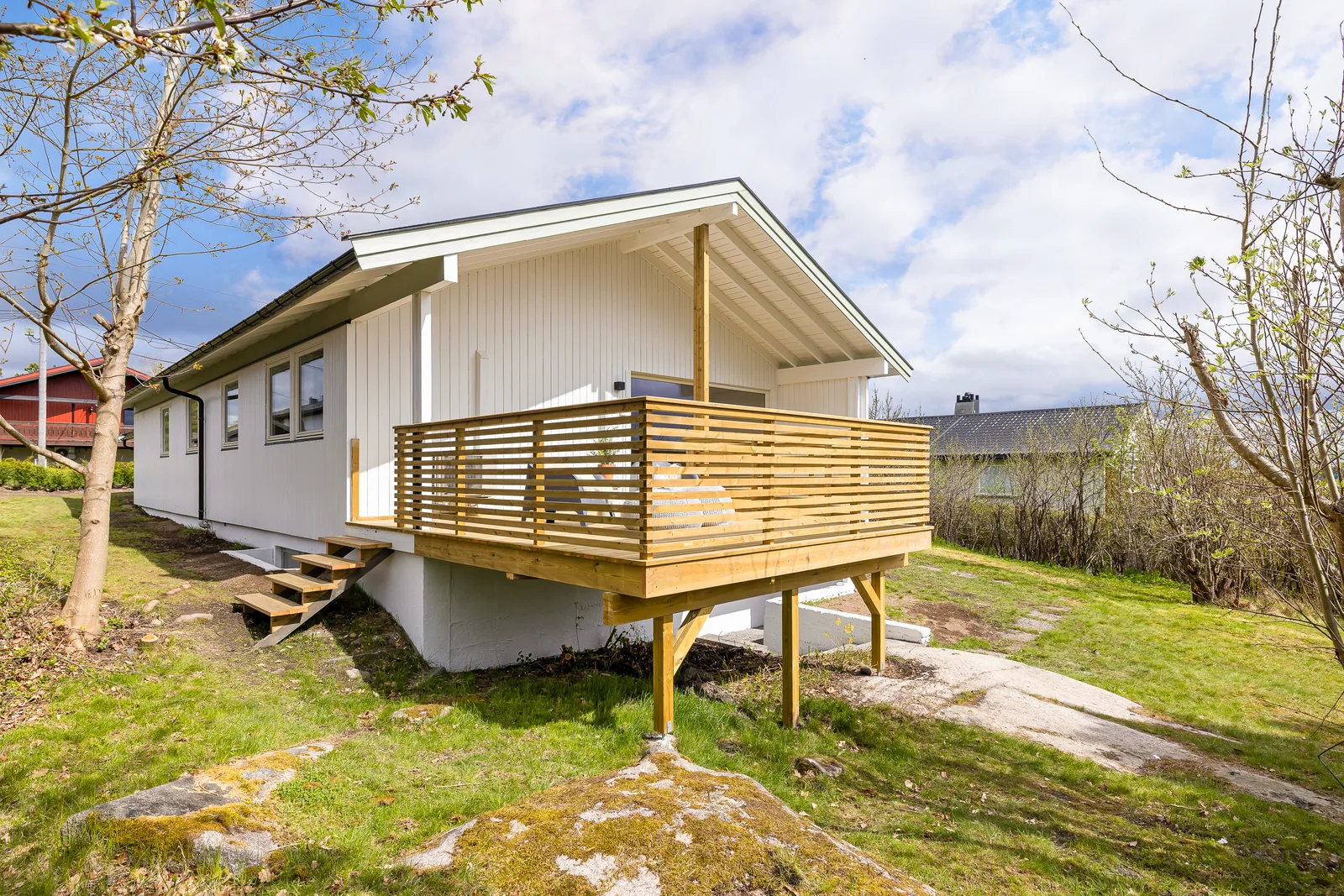 Hvit enebolig med trekledning, overbygd terrasse og rekkverk i tre